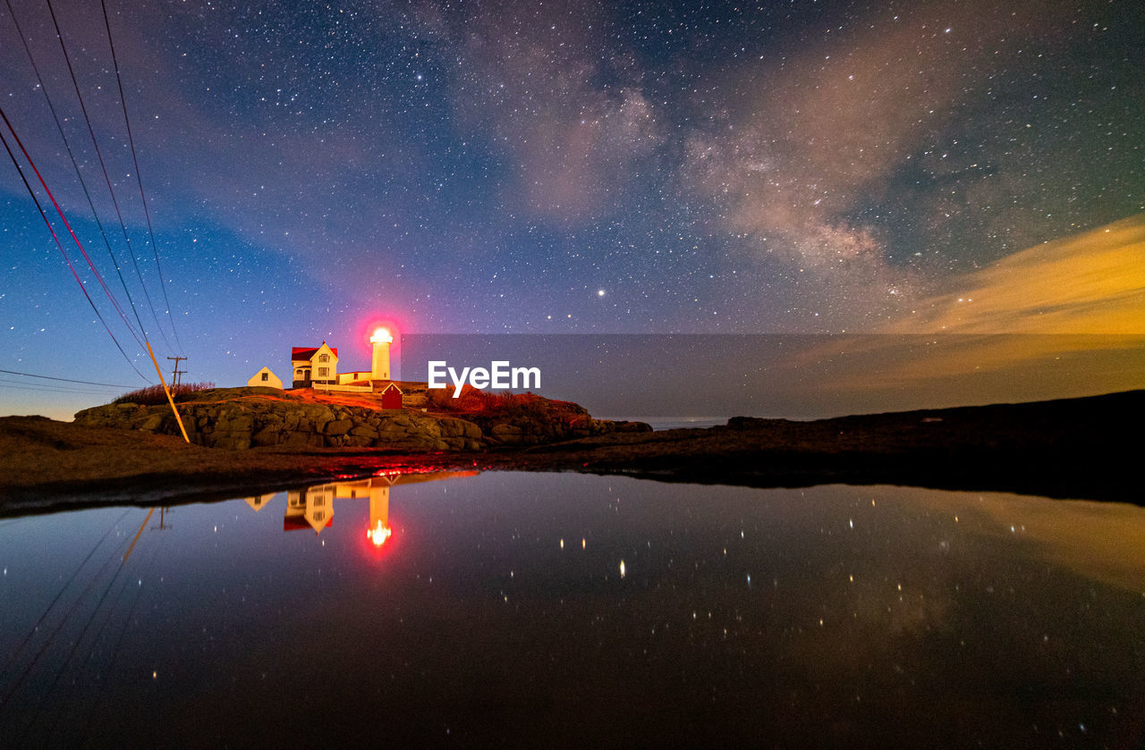 Lighthouse reflecting in water under the night sky milky way.