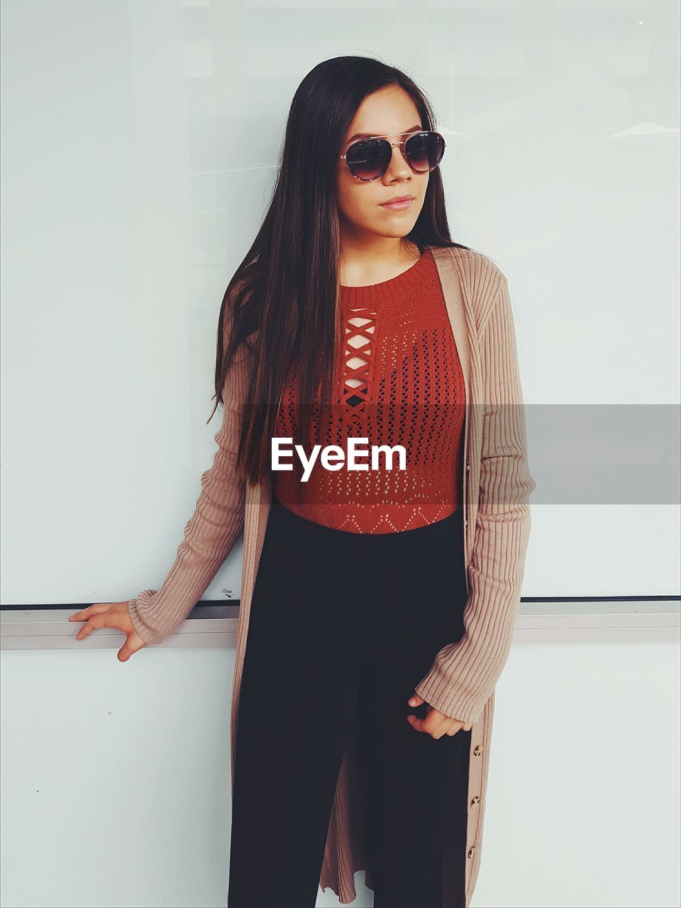 Young woman wearing sunglasses while standing by wall