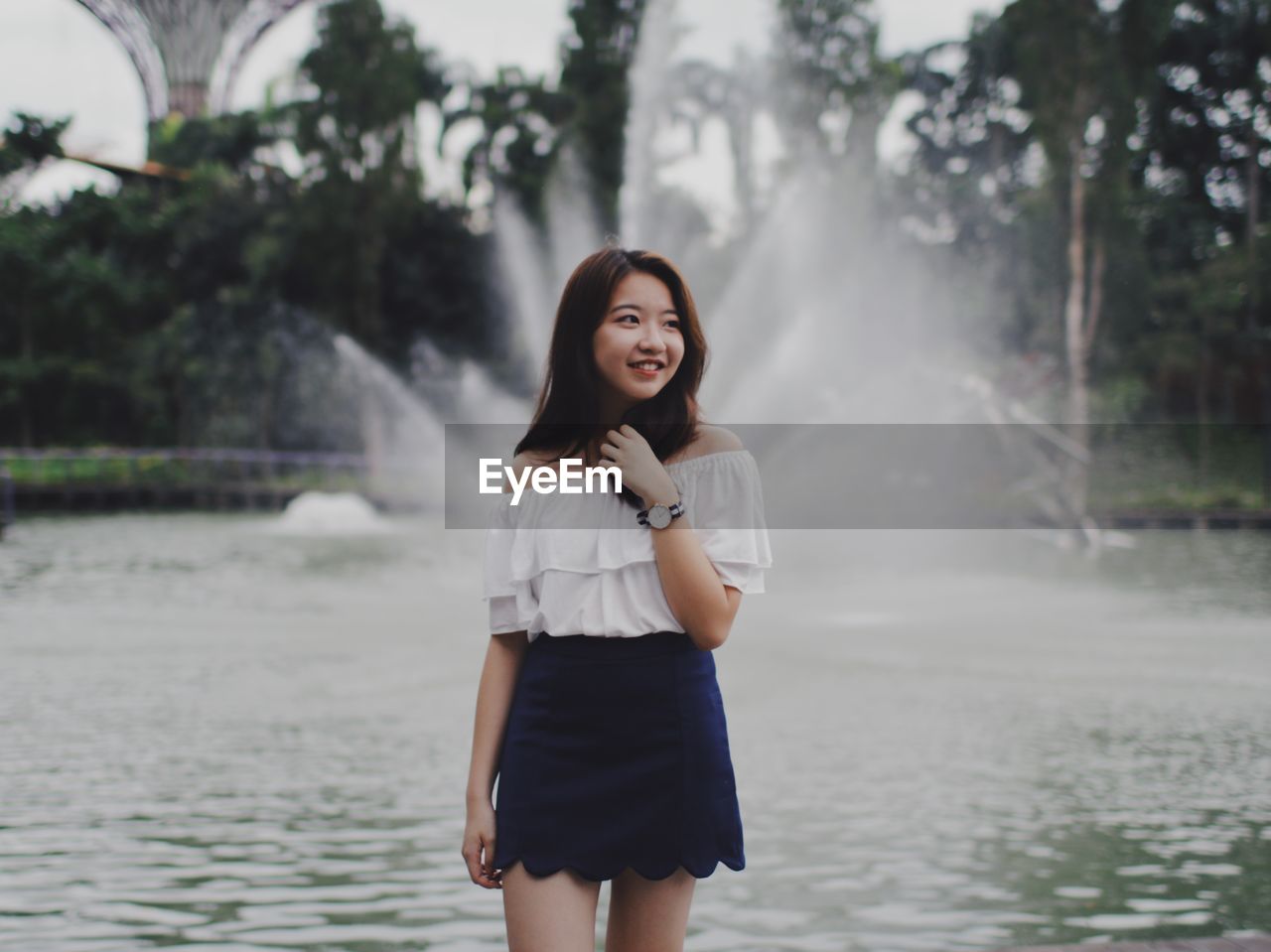 Smiling young woman standing against fountain at park
