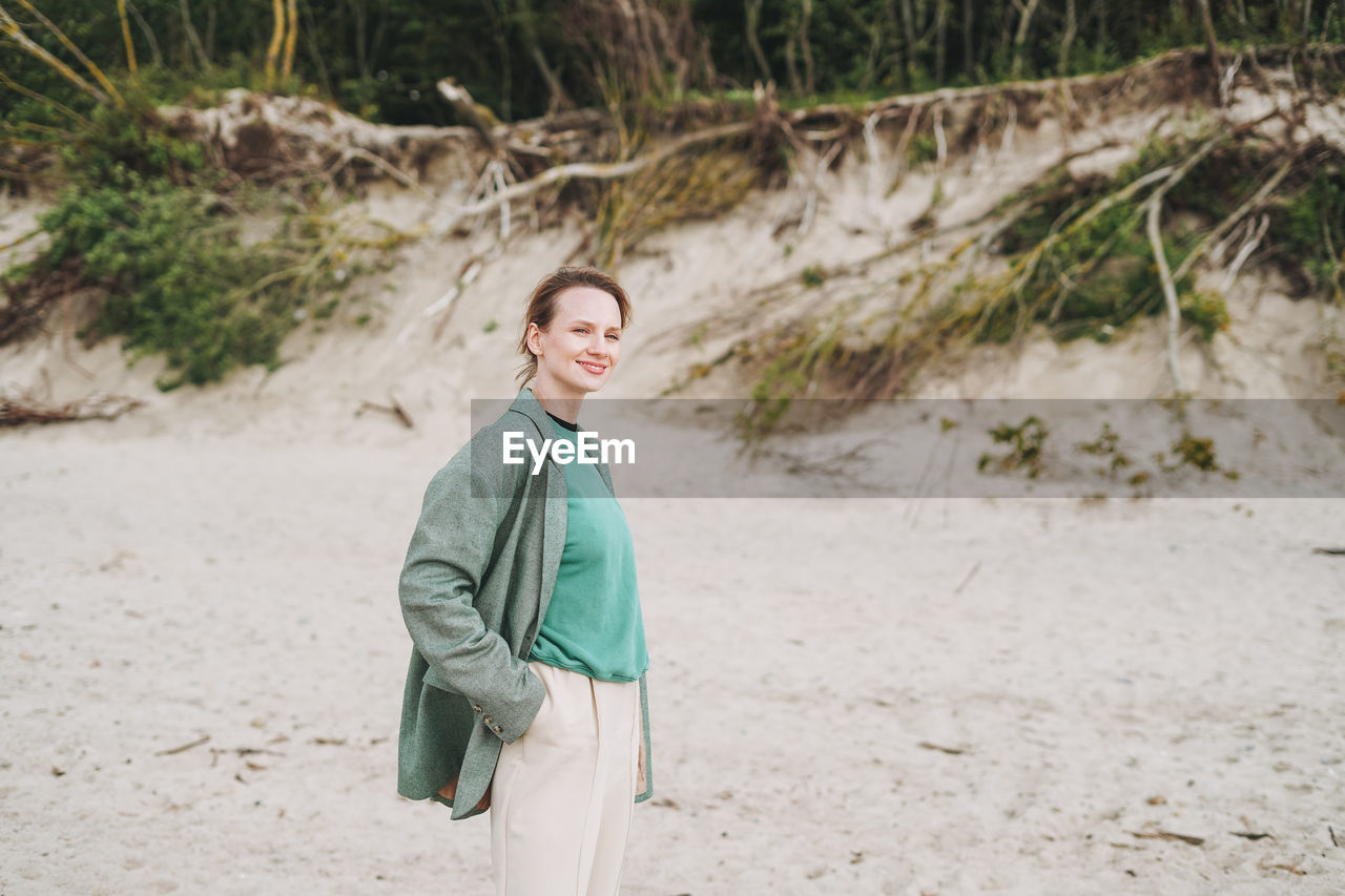 Stylish young woman in a green suit on a sandy beach