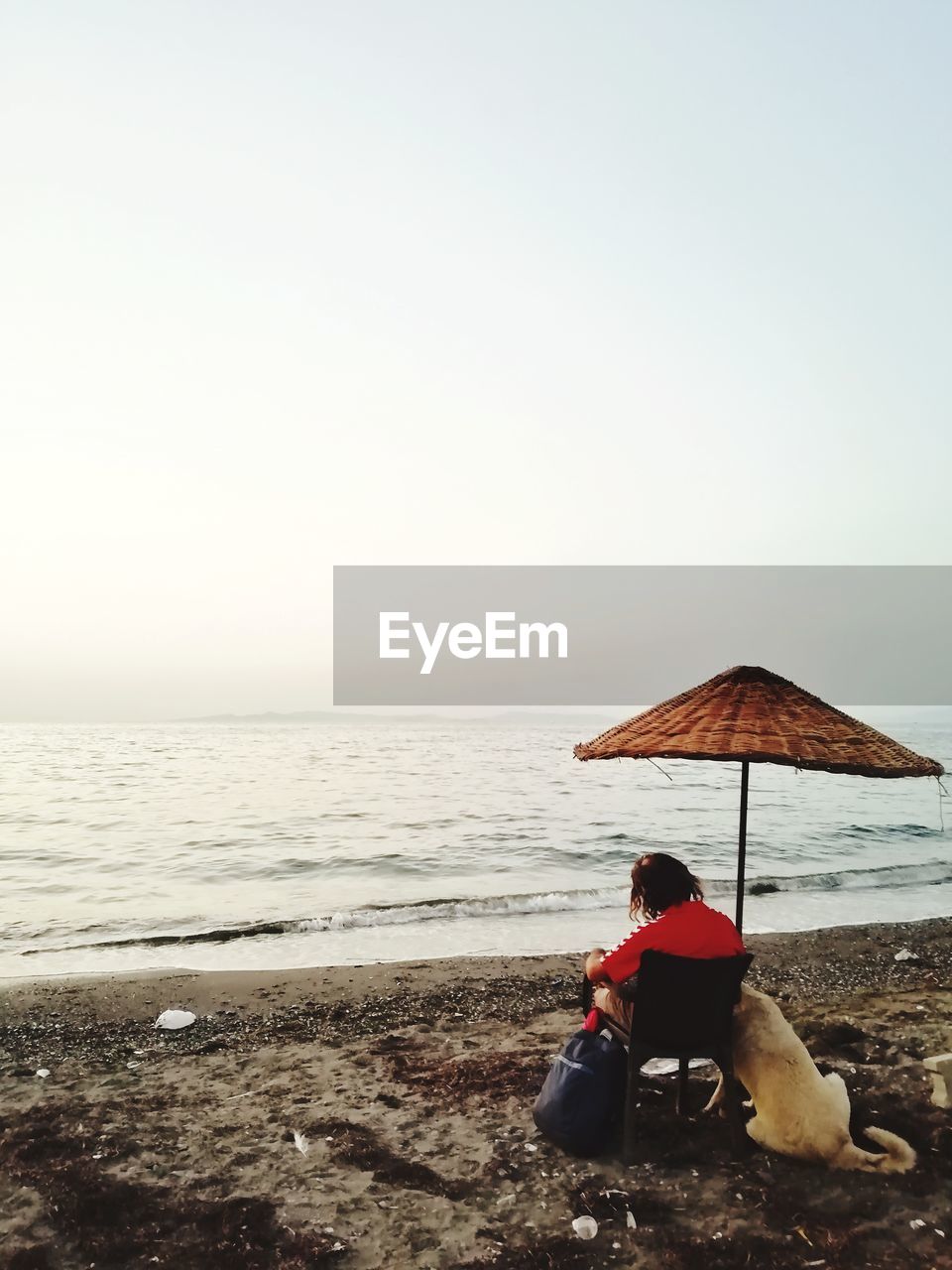 VIEW OF PEOPLE SITTING ON BEACH AGAINST CLEAR SKY