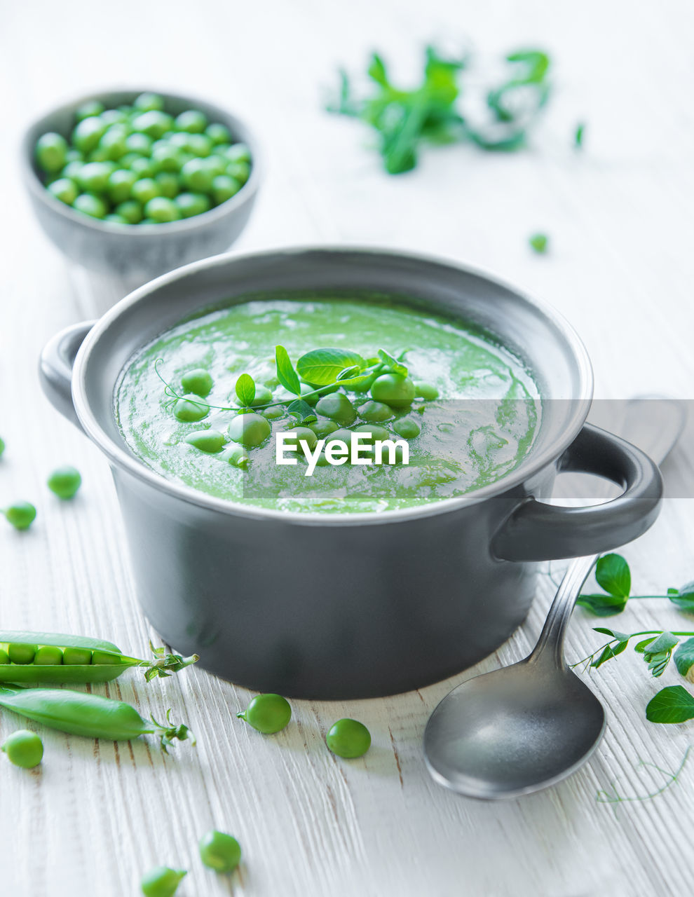 Fresh green pea soup bowl on white wooden background