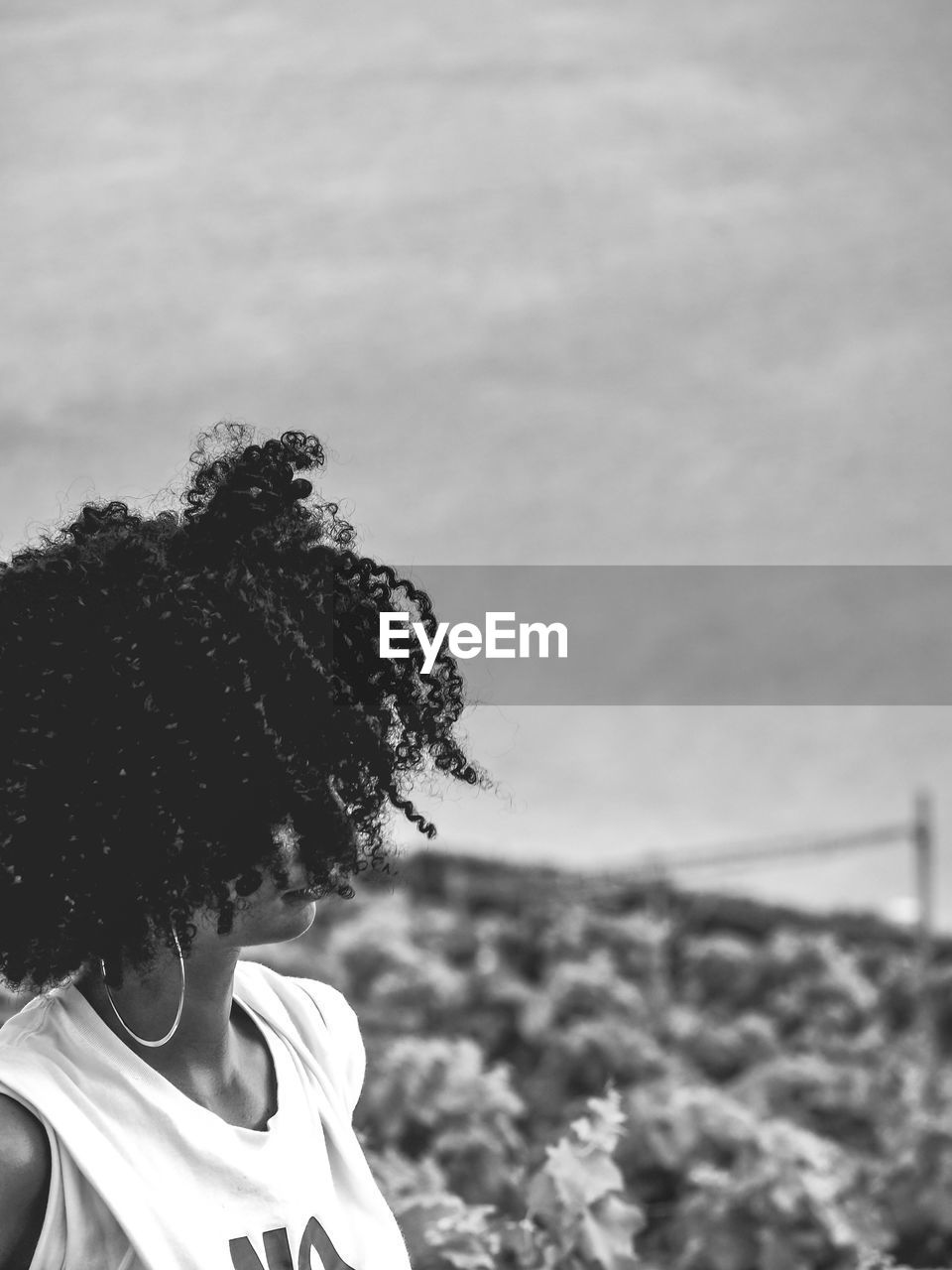 Close-up of woman with curly hair standing against cloudy sky