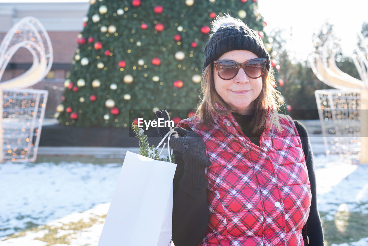 Portrait of woman standing against christmas tree during winter