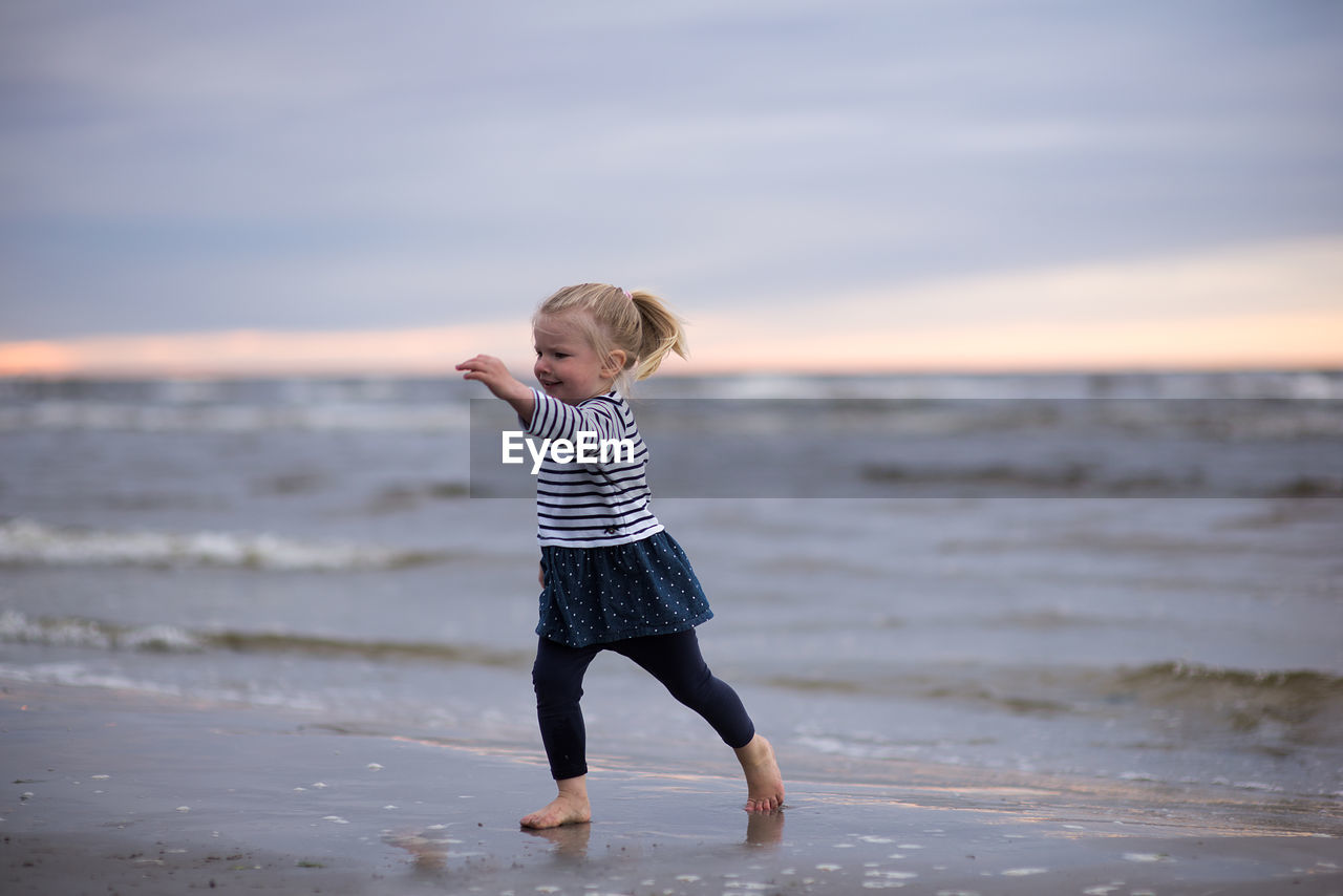 Full length of girl playing at beach against sky during sunset