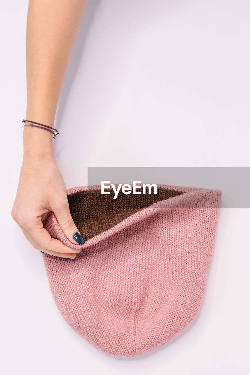 Hand of caucasian woman hold bilateral pink-brown knitted beanie hat. flat lay, copy space. 