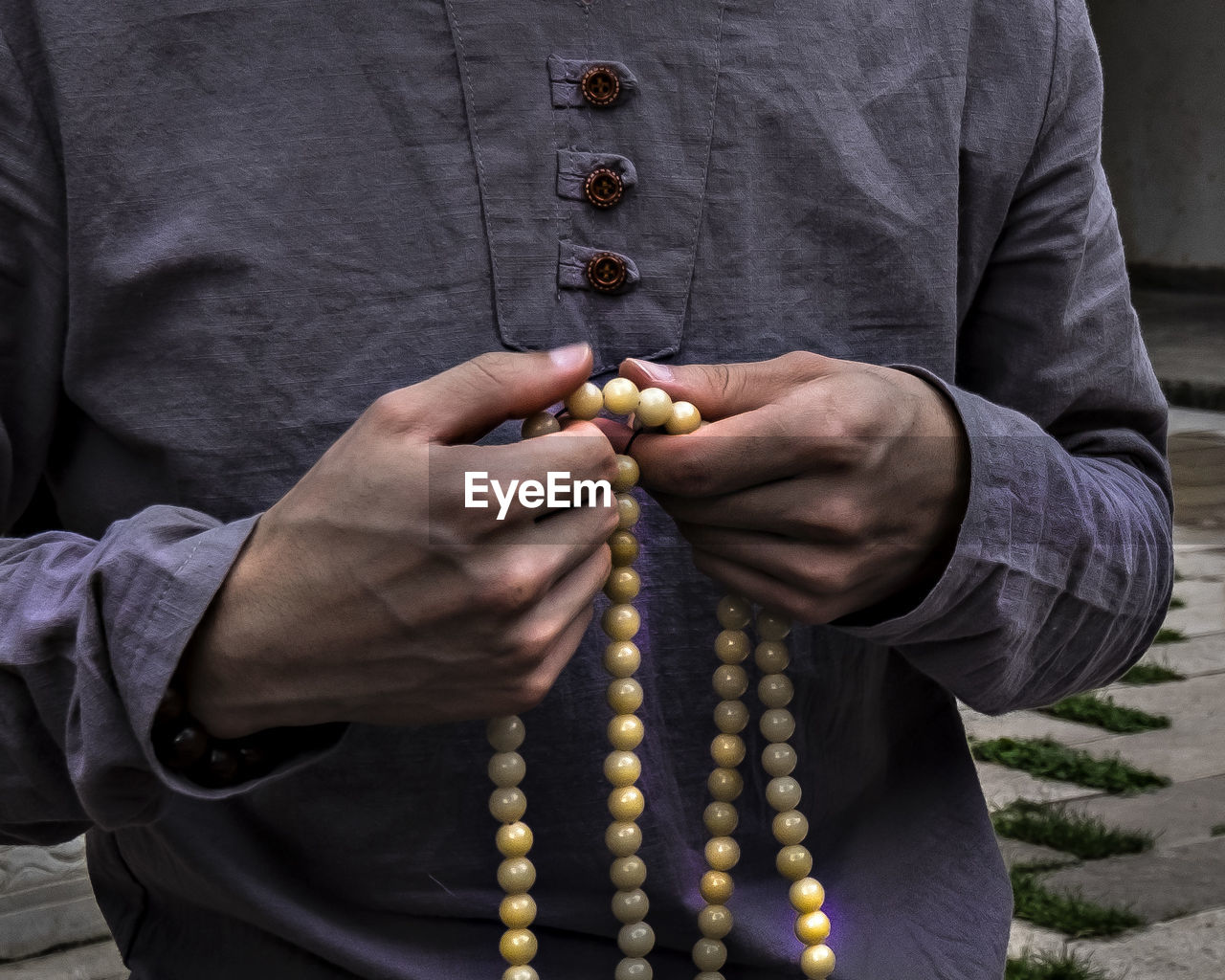 Midsection of man holding religious beads while standing outdoors