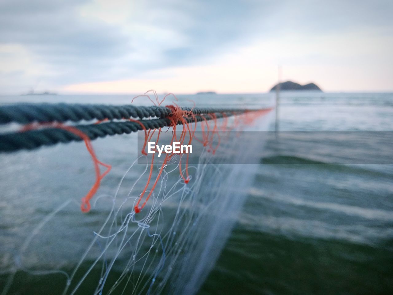 CLOSE-UP OF FISHING NET AGAINST SEA DURING SUNSET