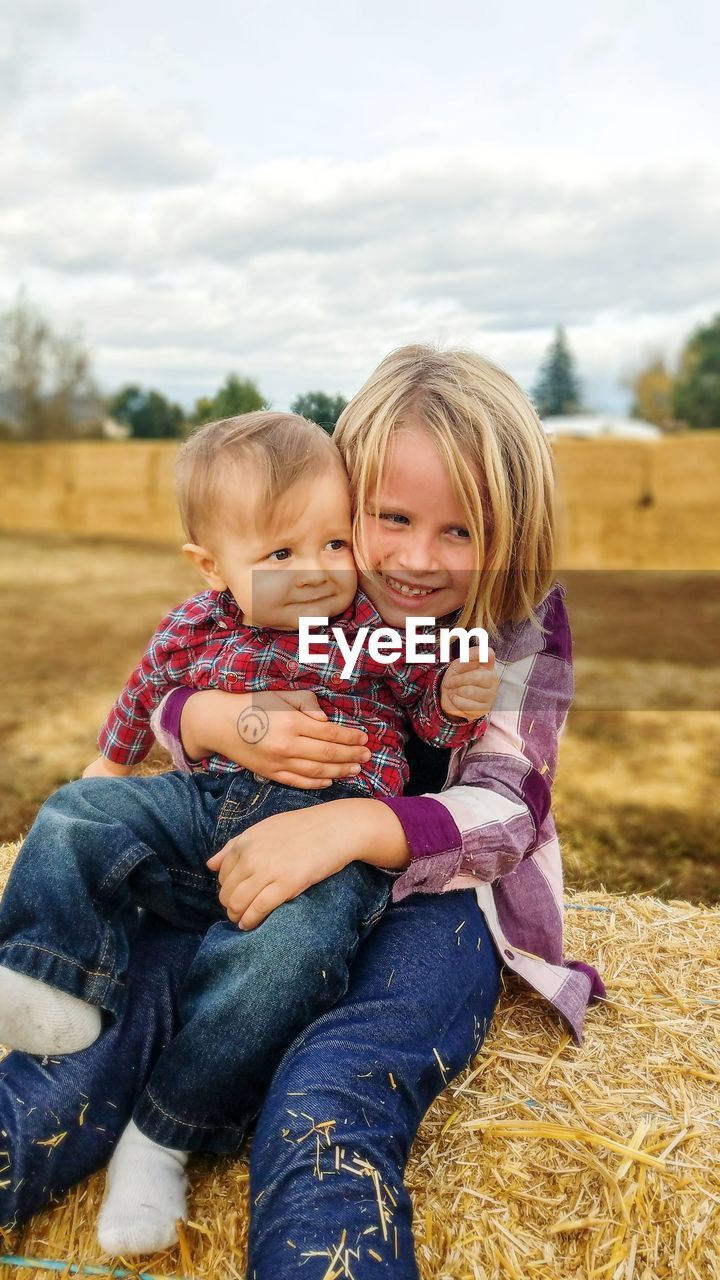 Smiling girl with brother sitting on haystack