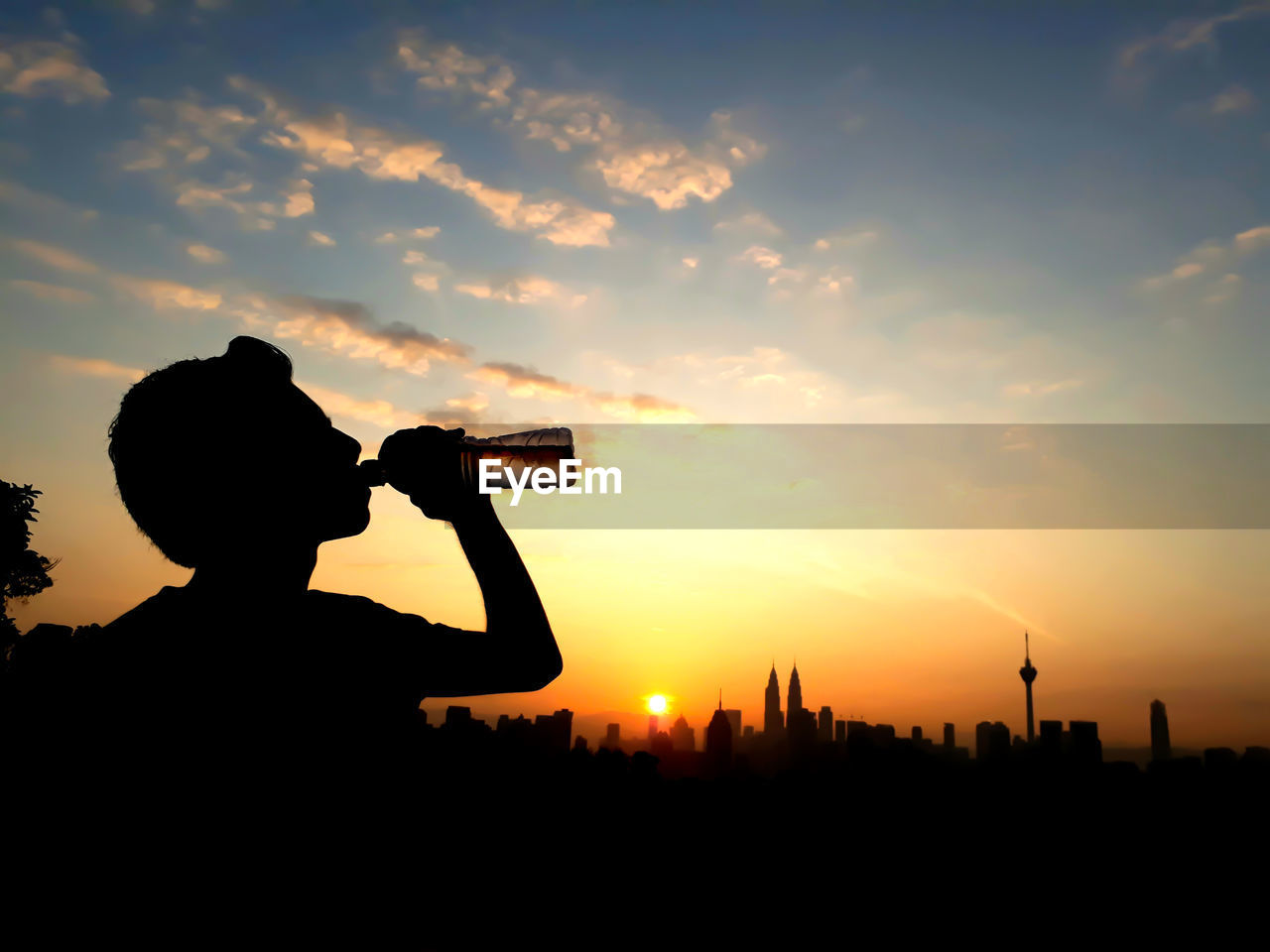 Silhouette man drinking water against sky during sunset