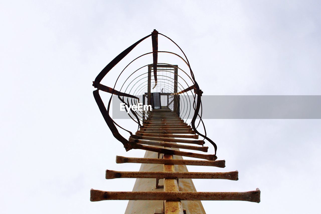 Low angle view of rusty ladder on pole against sky