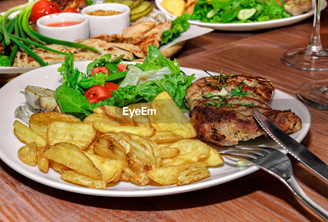 Table with various meat and vegetable dishes and fried potatoes