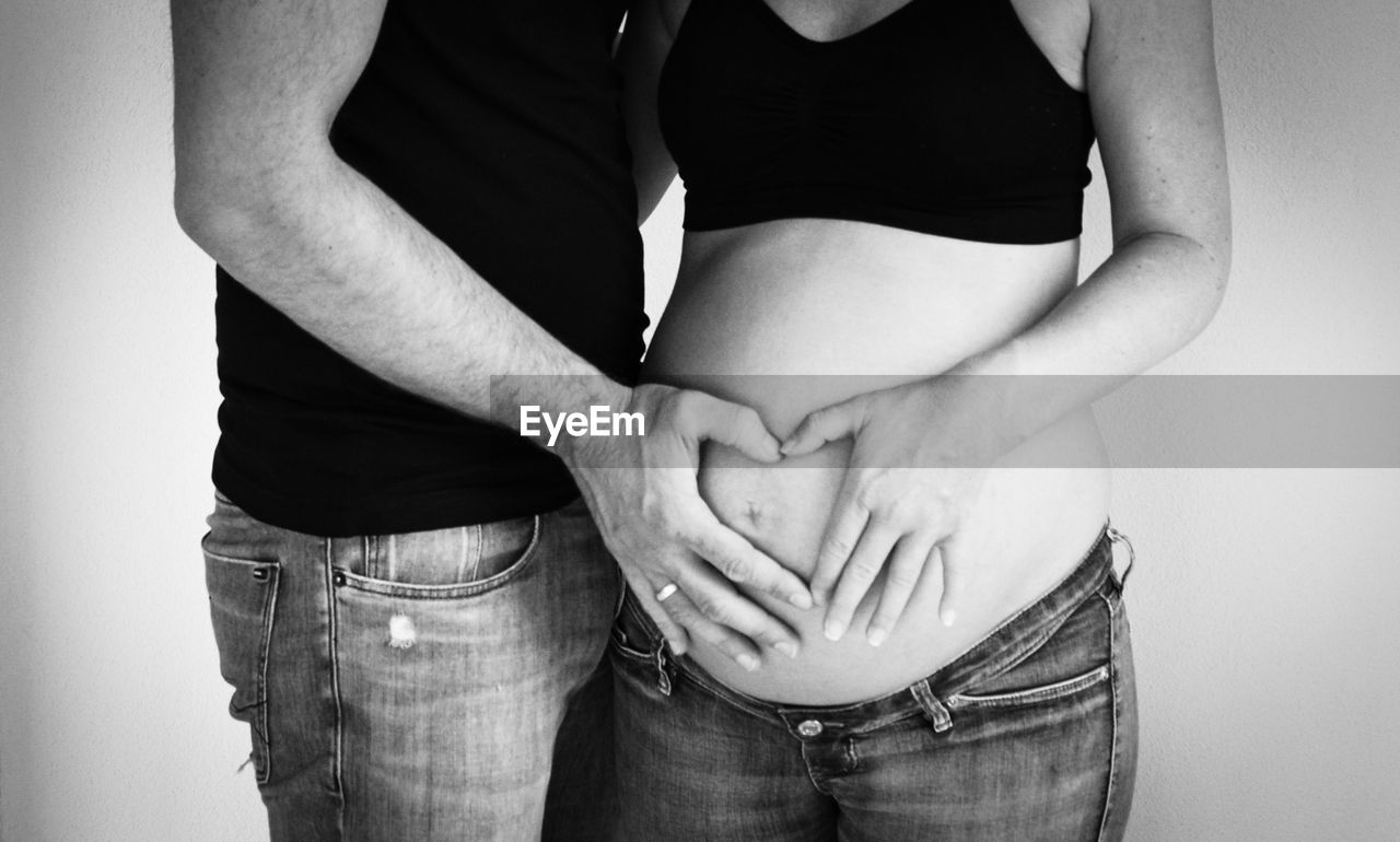 Midsection of man standing with pregnant woman against wall