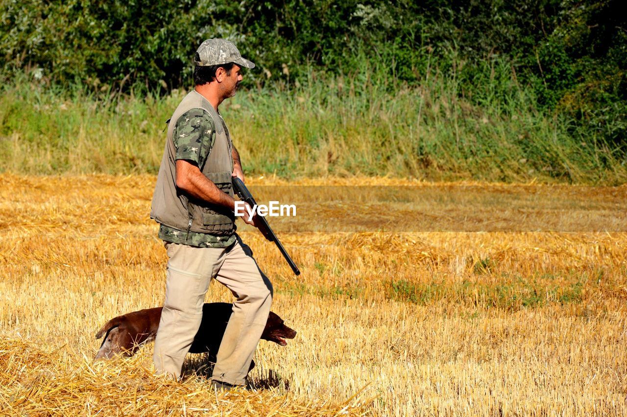 Side view of hunter walking with dog on land