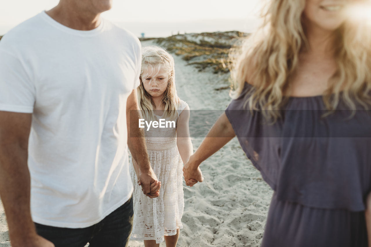 Serious girl making sad face walking with parents at beach