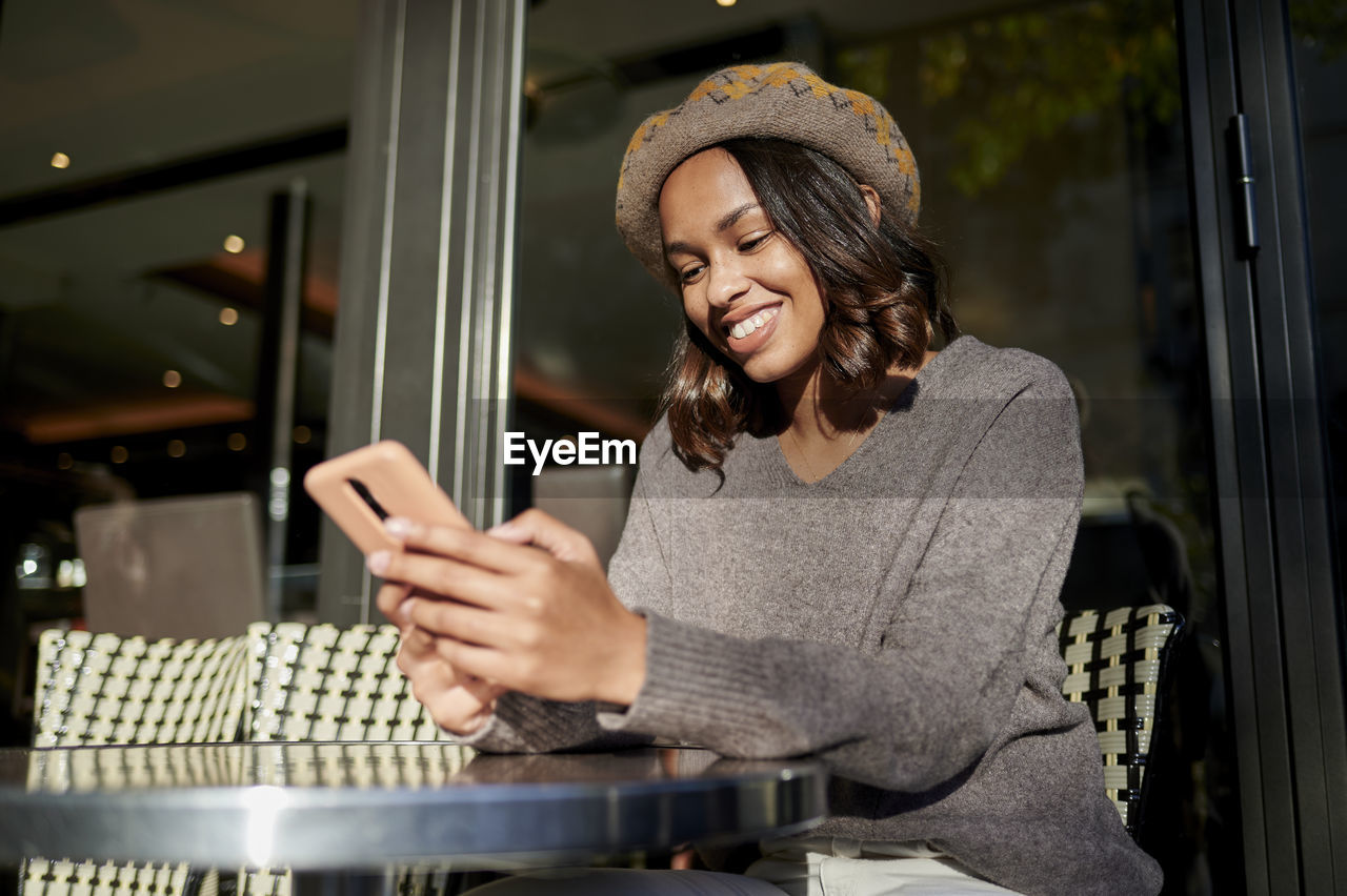 Smiling woman using smart phone at sidewalk cafe