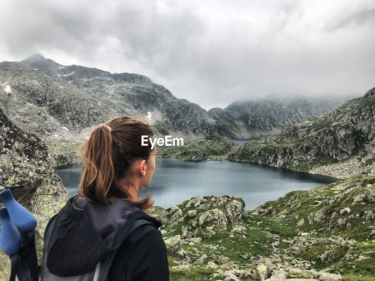 Woman looking at lake and mountains against cloudy sky
