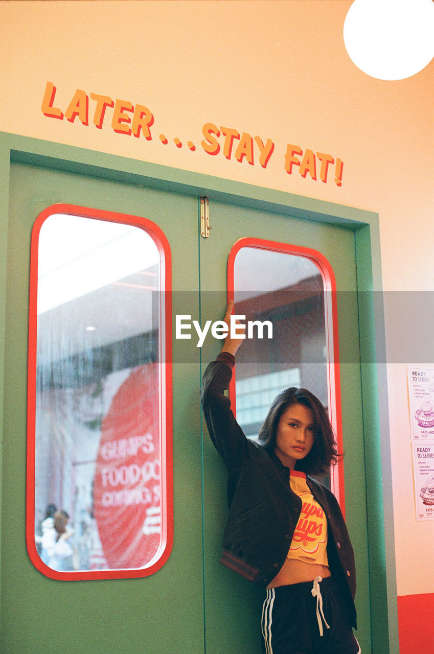 PORTRAIT OF YOUNG WOMAN STANDING BY TEXT ON WALL