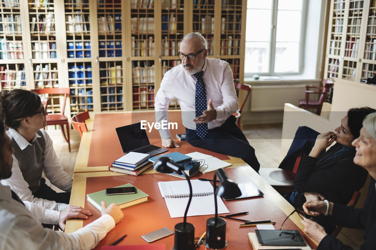 Confident male professional discussing with coworkers sitting at table in law library