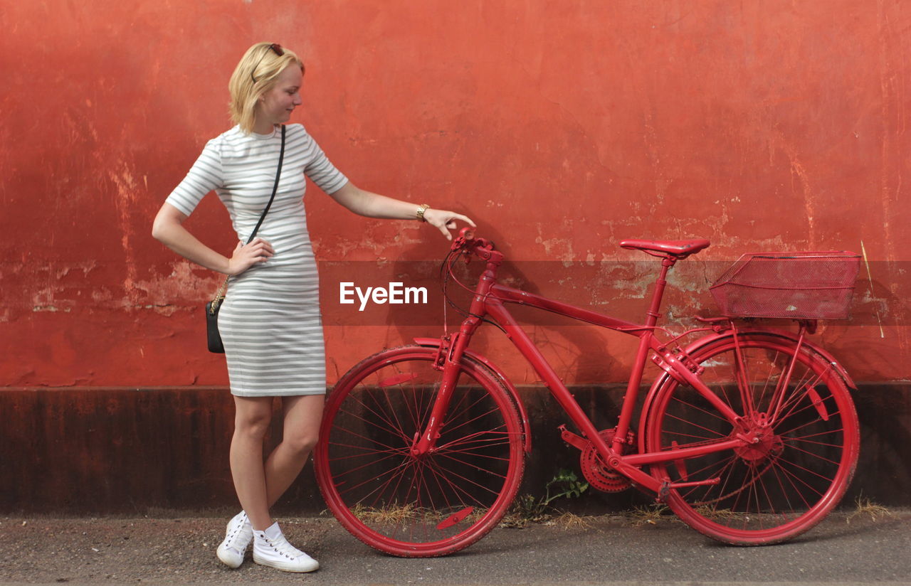 Full length of woman holding red bicycle while standing against wall
