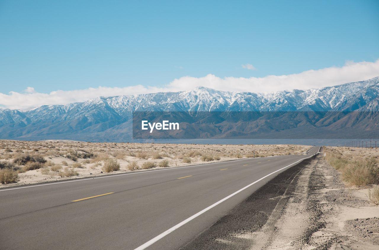 Road by mountains against sky during winter