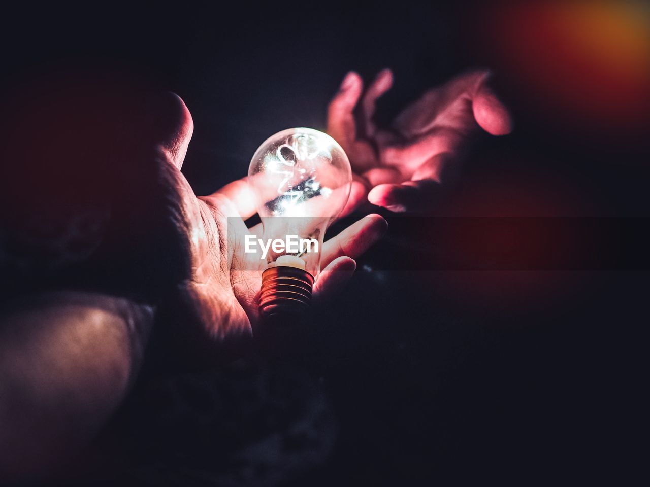 Digital composite image of hand holding illuminated light bulb in darkroom