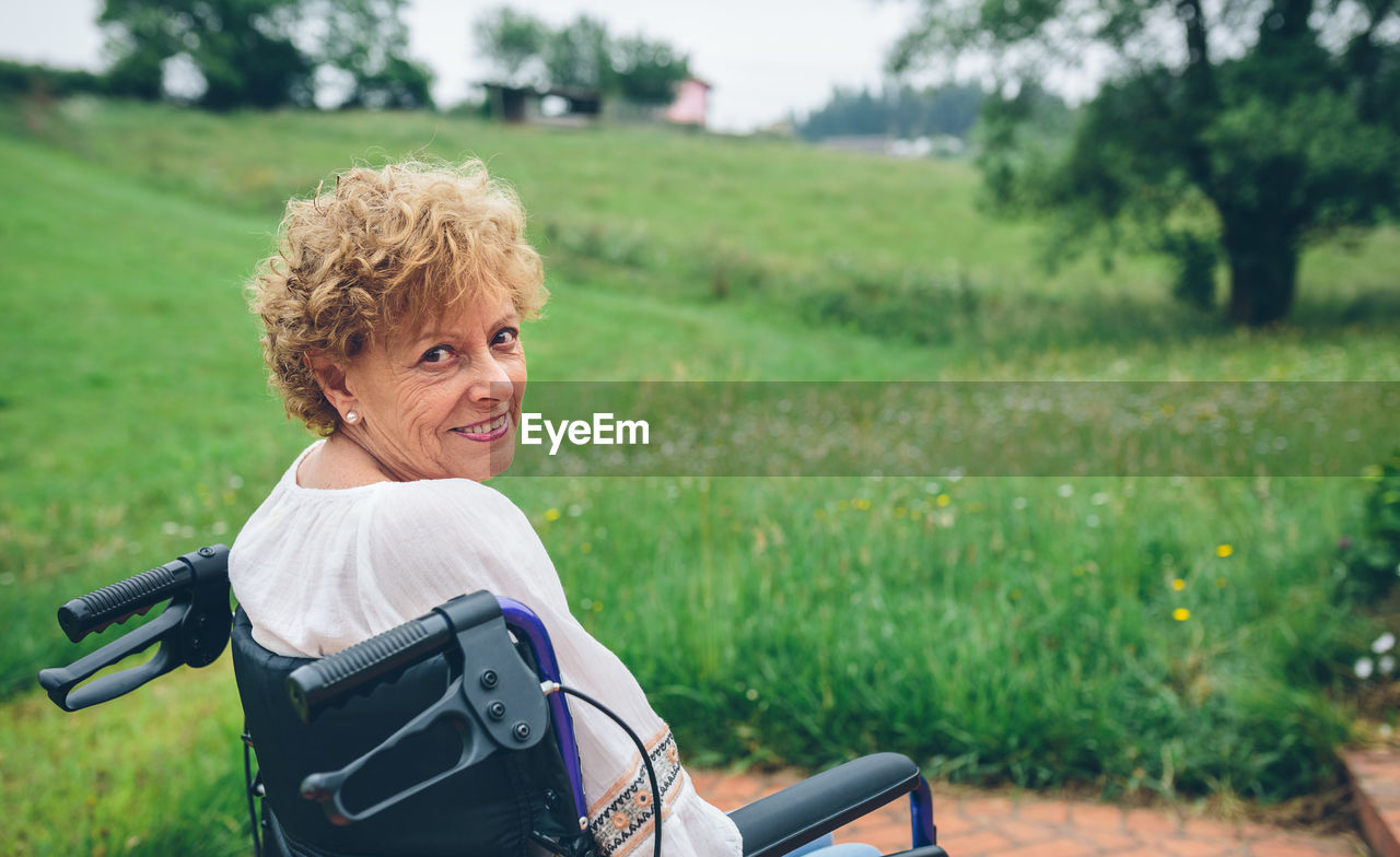 Portrait of smiling senior woman sitting on wheelchair at park