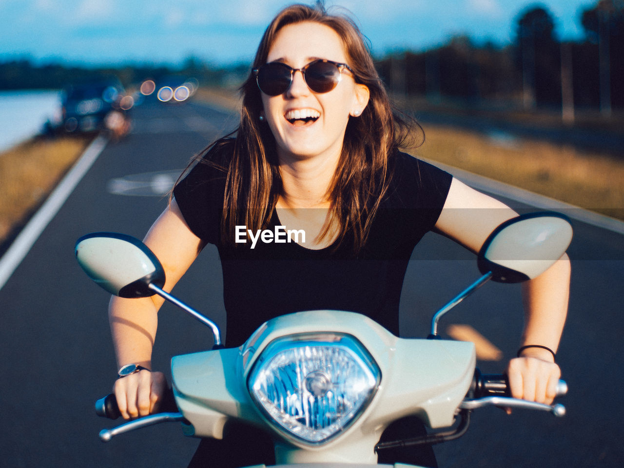 Smiling young woman sitting on motor scooter at road