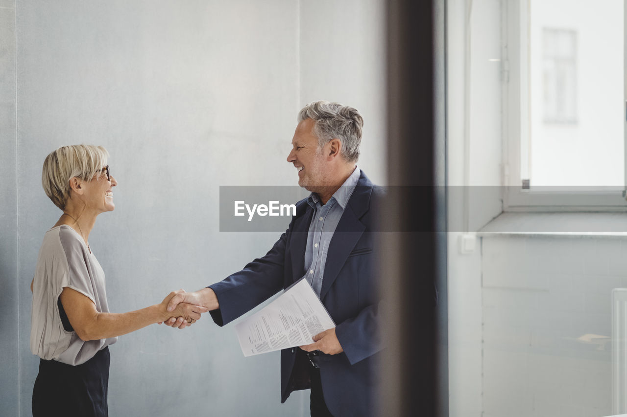 Mature businessman and businesswoman shaking hands in new office