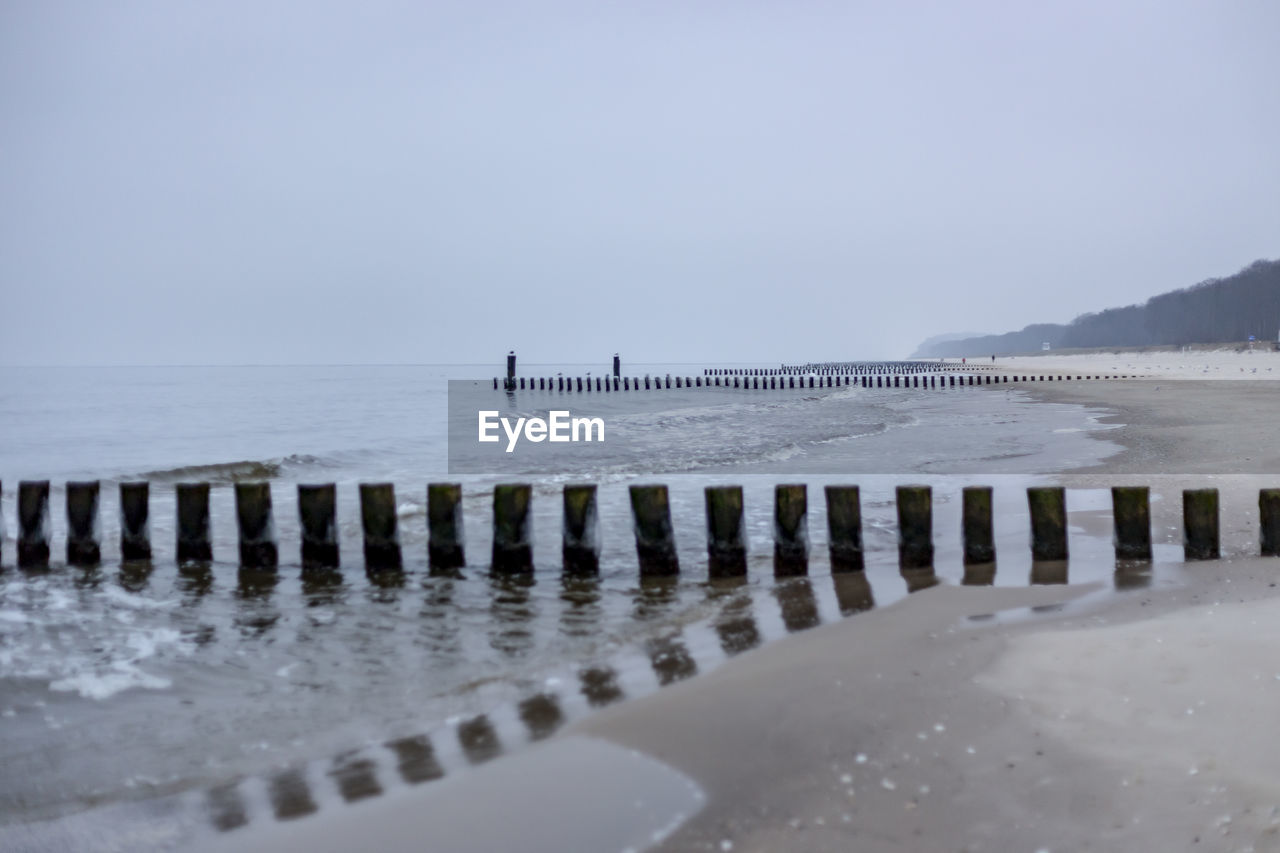 WOODEN POSTS ON BEACH AGAINST SKY