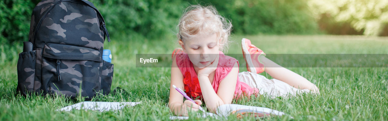 Cute girl doing homework while lying on grass at park