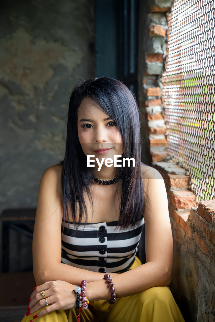 Portrait asian woman lookinging at a camera next to brick wall.