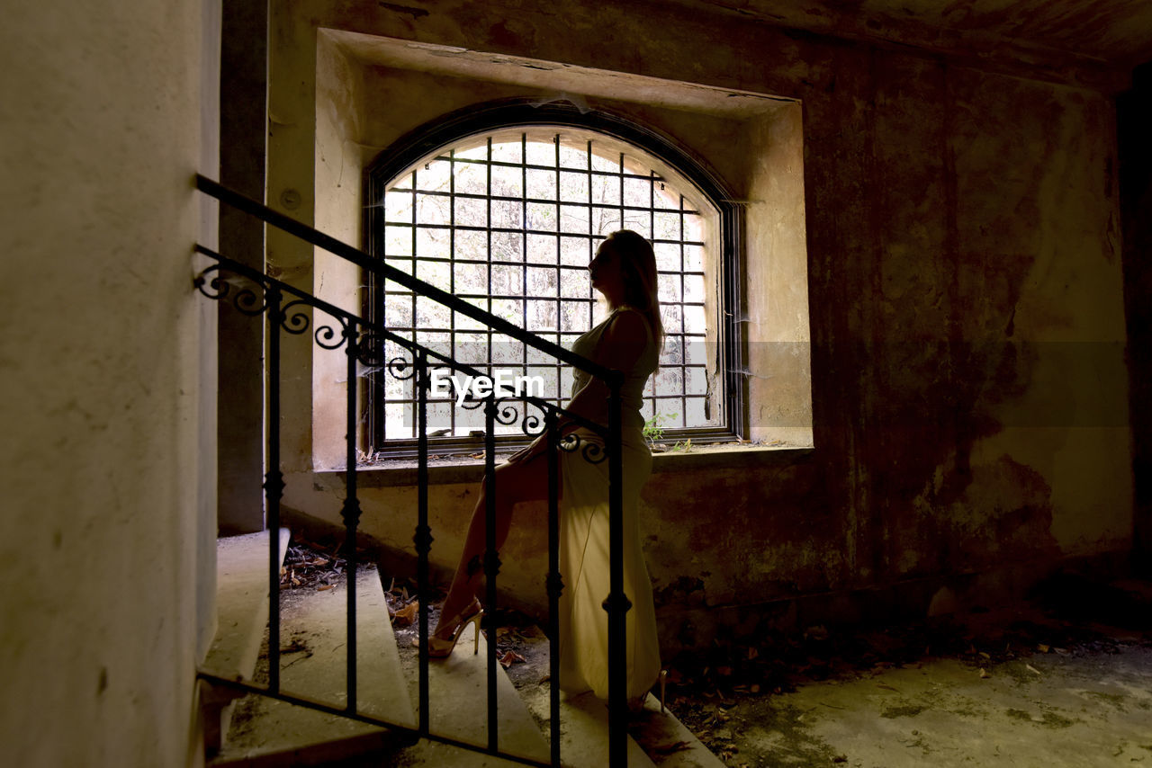 FULL LENGTH OF WOMAN STANDING IN ABANDONED BUILDING