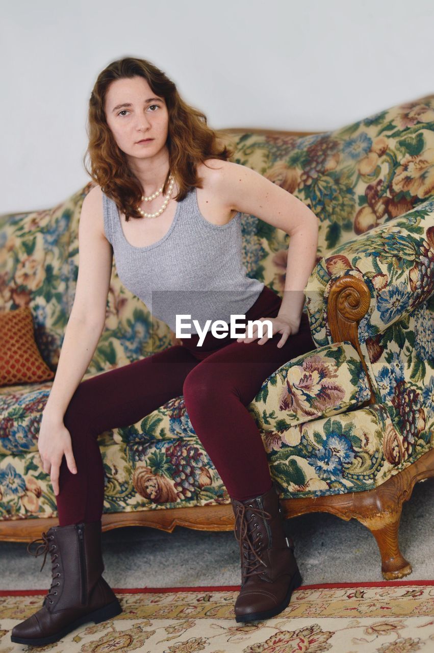 PORTRAIT OF BEAUTIFUL YOUNG WOMAN SITTING ON SOFA AT HOME