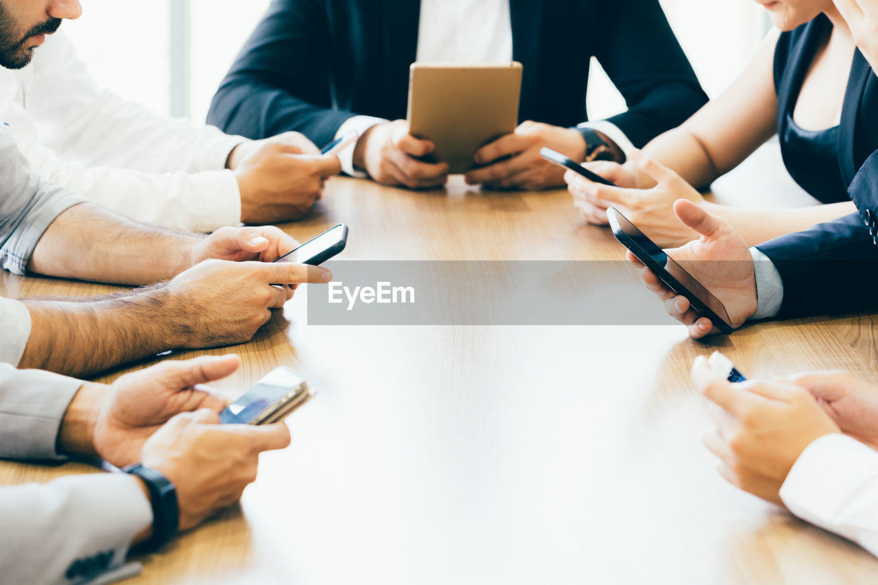 Midsection of business colleagues using phones at table in office