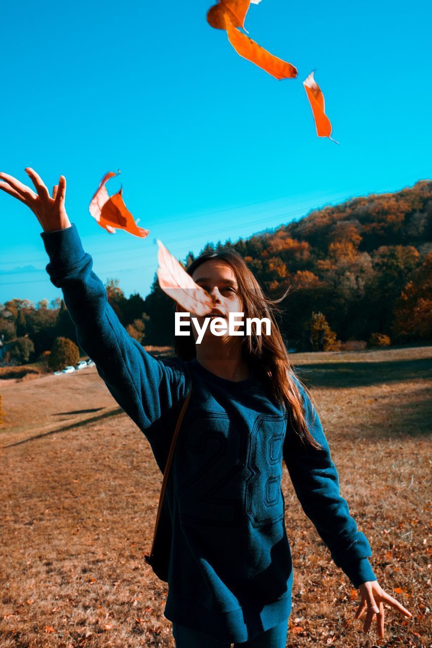 Girl throwing autumn leaves while standing on land