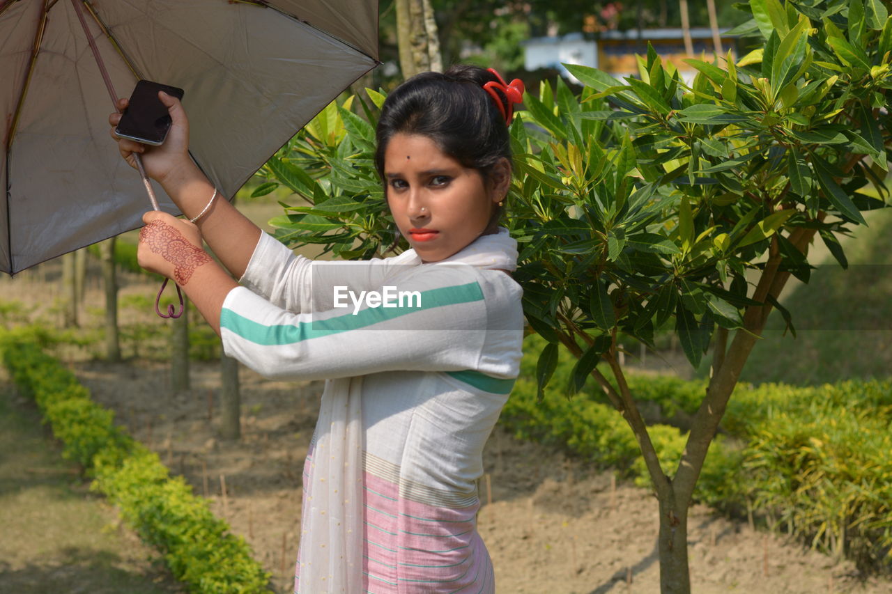 PORTRAIT OF BEAUTIFUL WOMAN STANDING BY PLANTS