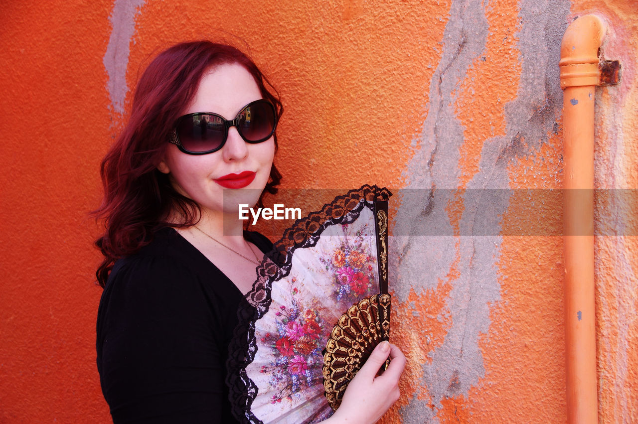 Portrait of woman with folding fan by orange wall