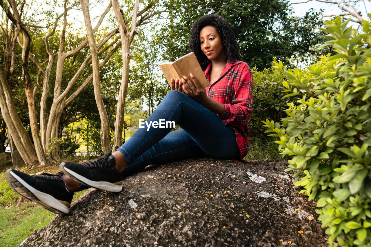 portrait of young woman using mobile phone while sitting against plants