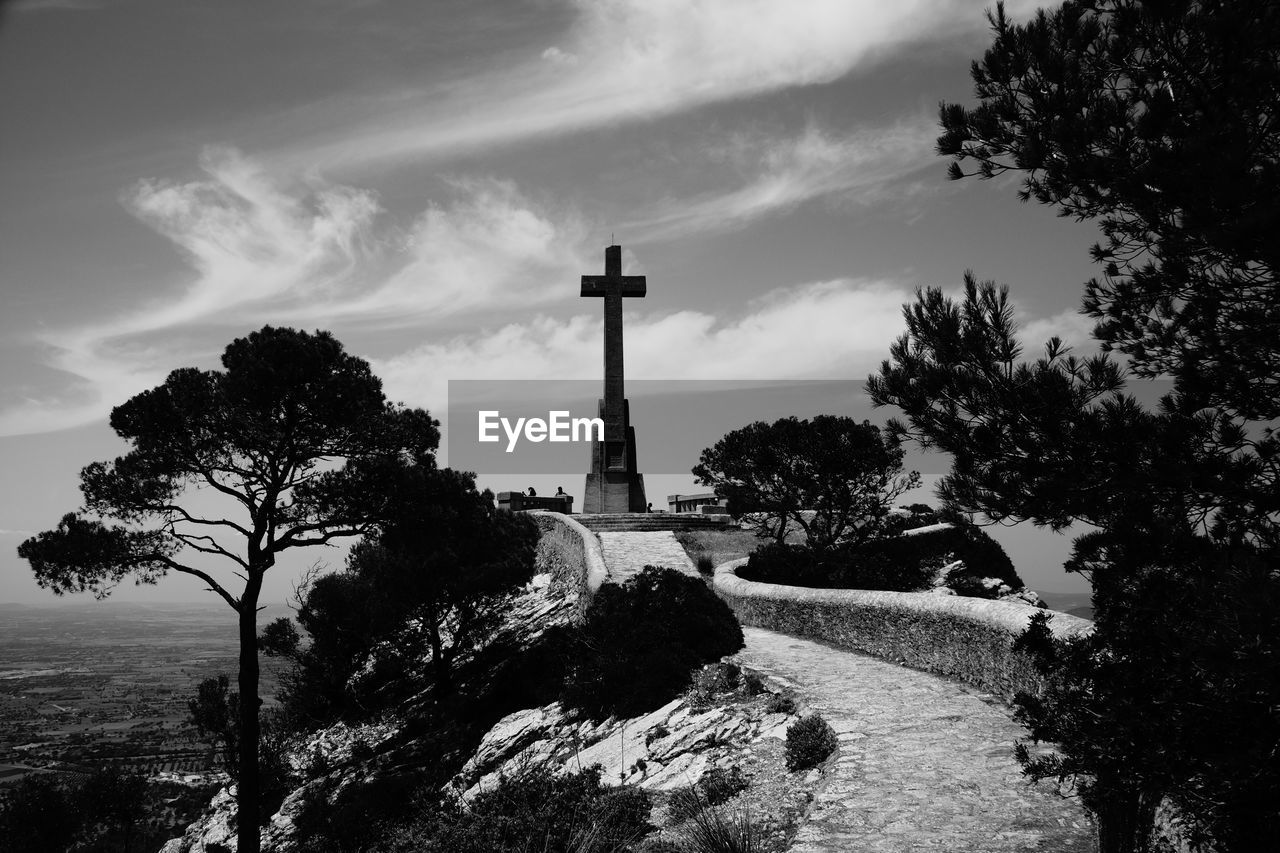 Cross on footpath against sky