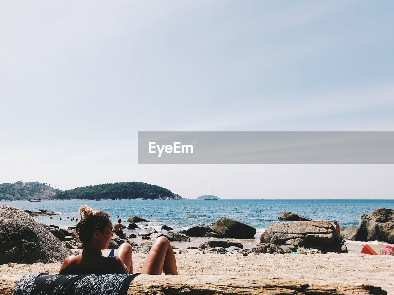 REAR VIEW OF WOMAN SITTING ON BEACH