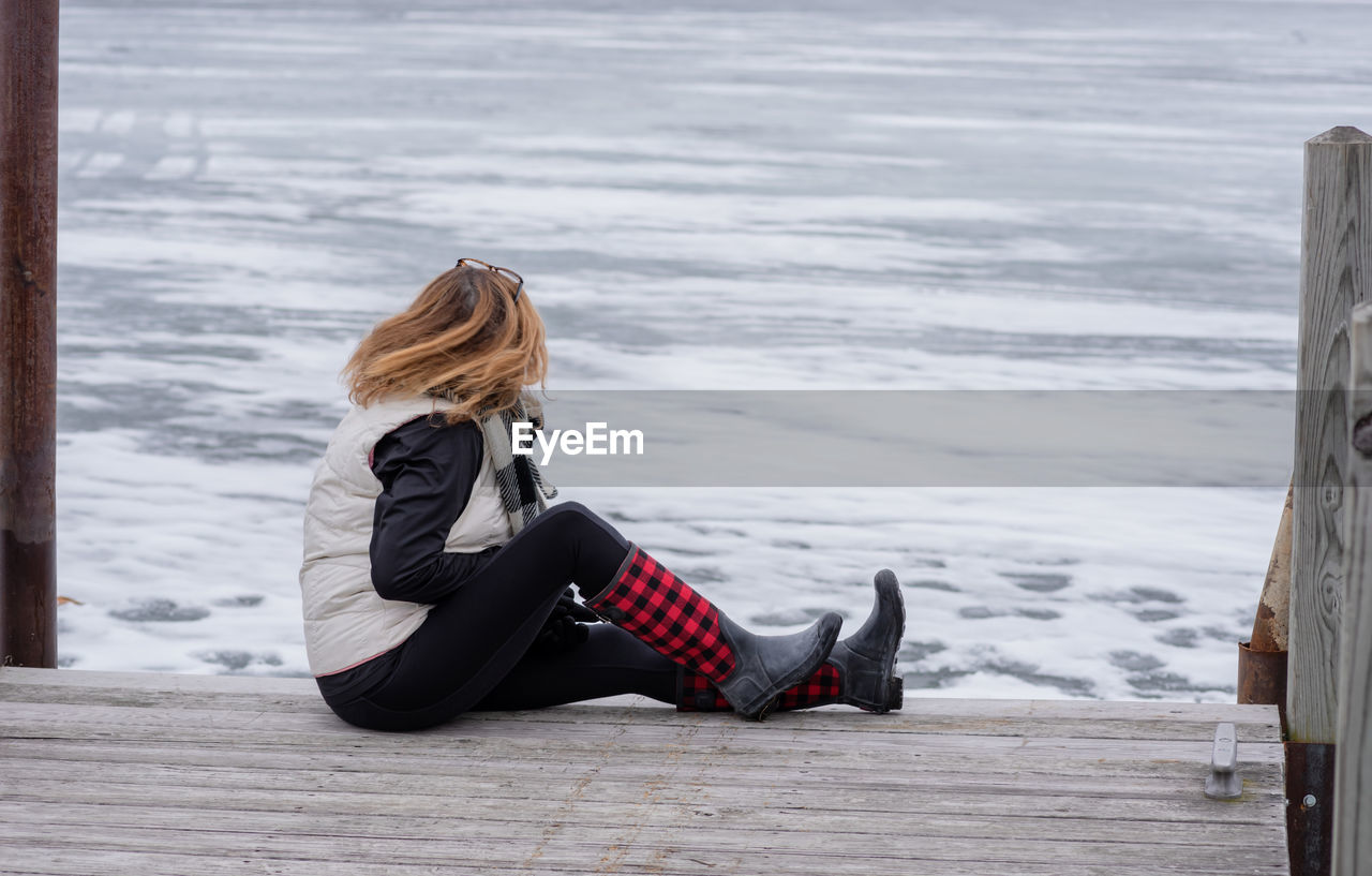 Full length of woman sitting on pier over frozen lake