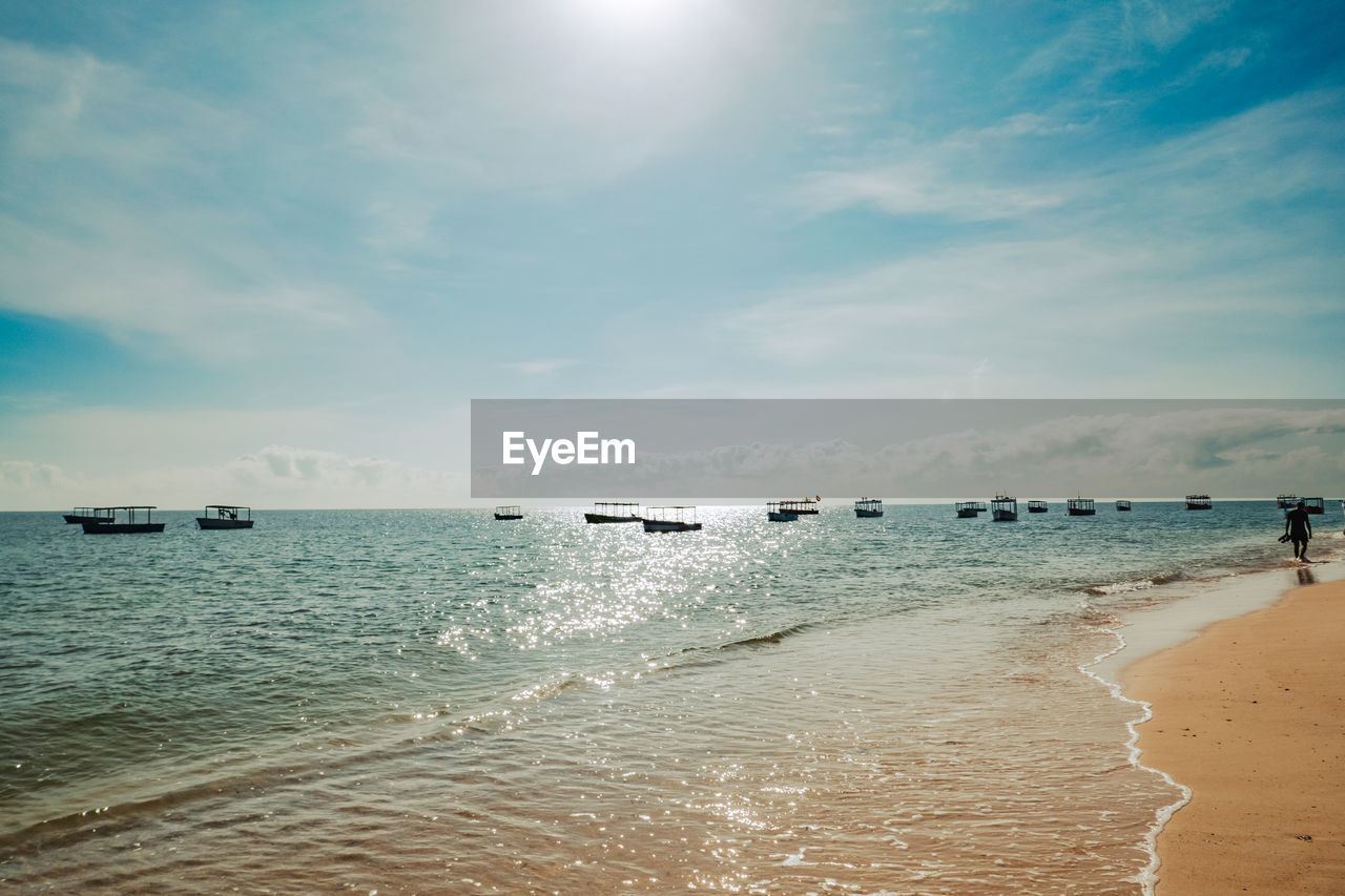 A man walking on the beach with fishing boats at the background at sunrise at malindi beach, kenya