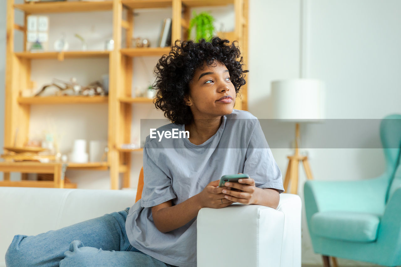 young woman using mobile phone while sitting on table at home