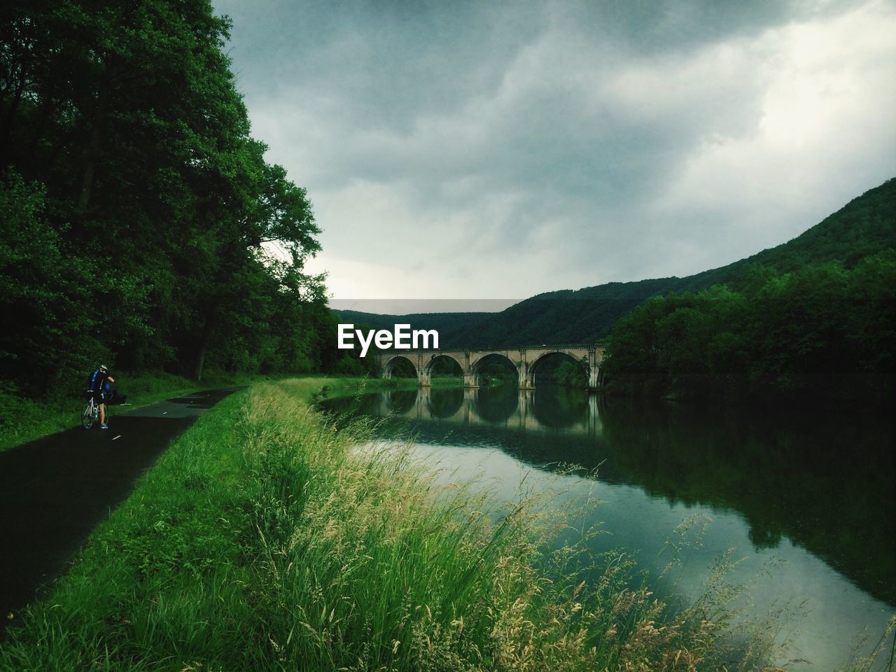 Reflection of arch bridge on calm river against cloudy sky