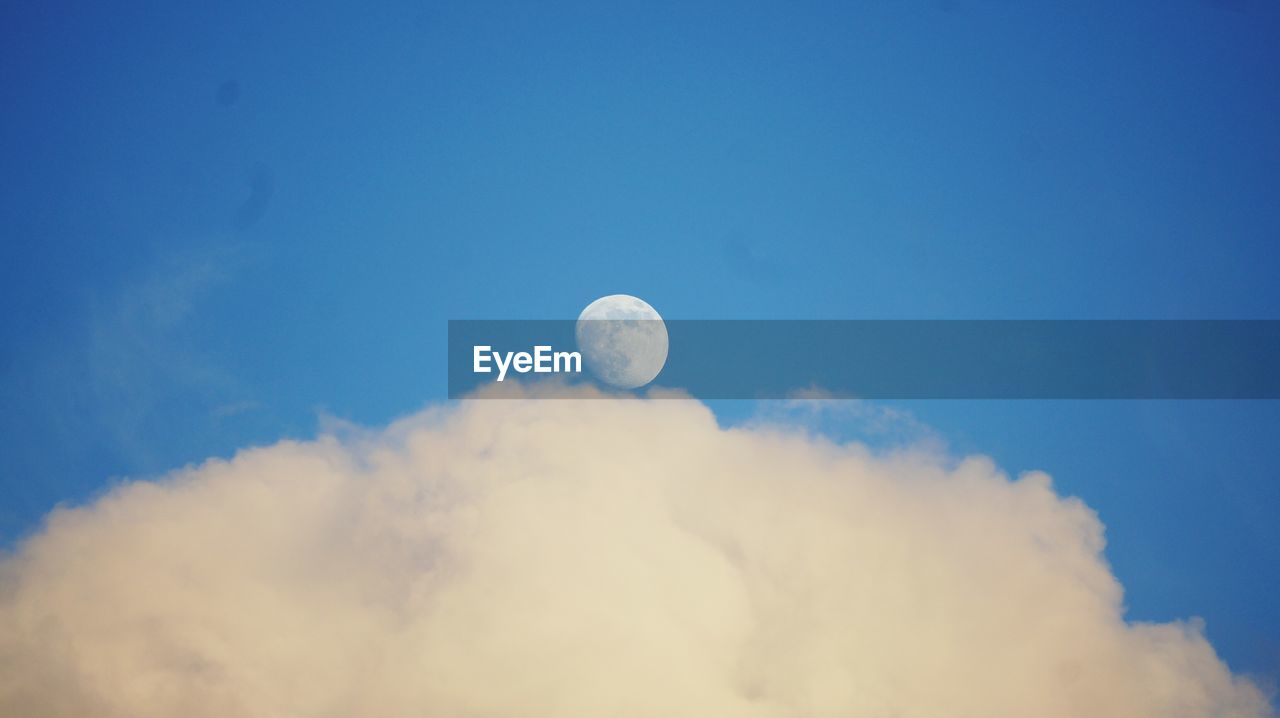 Low angle view of moon above cloud in blue sky