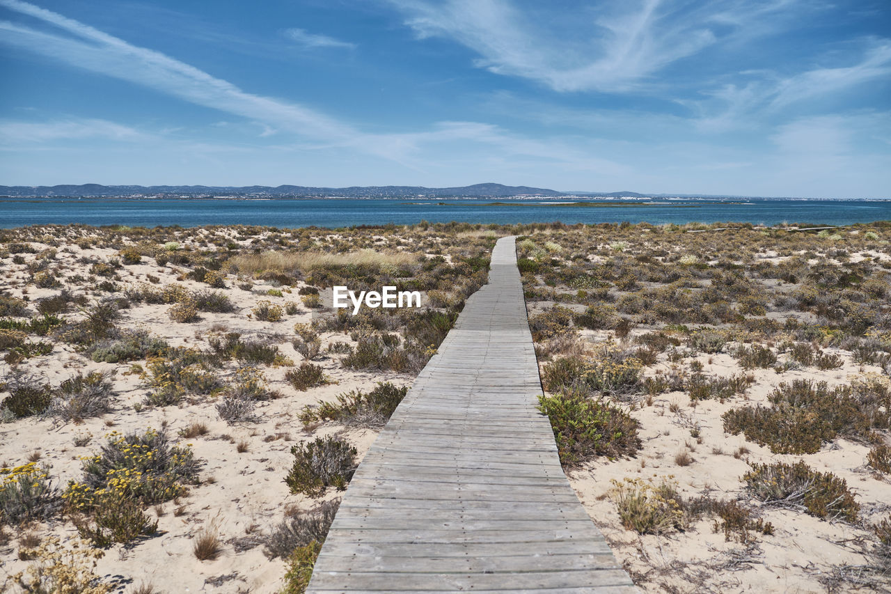 Footpath leading towards sea against sky