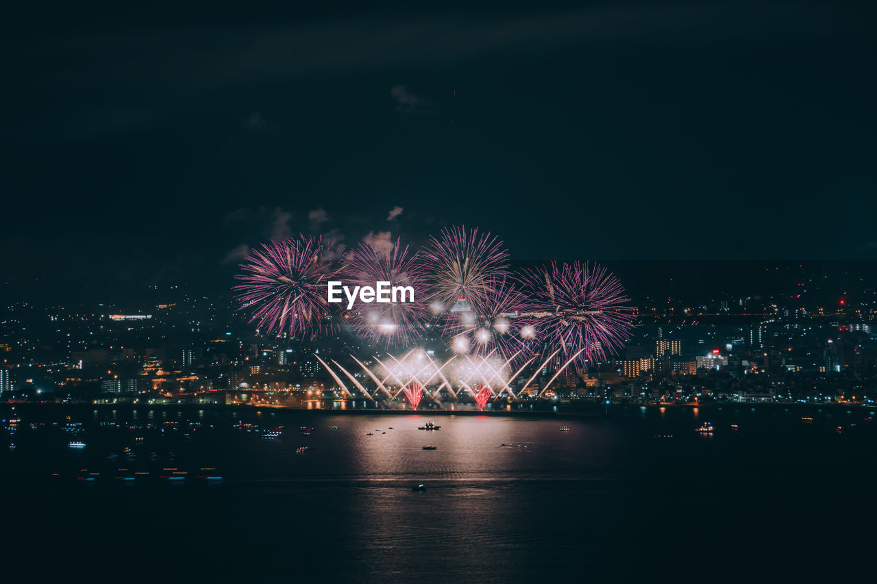 FIREWORK DISPLAY OVER ILLUMINATED CITY AGAINST SKY