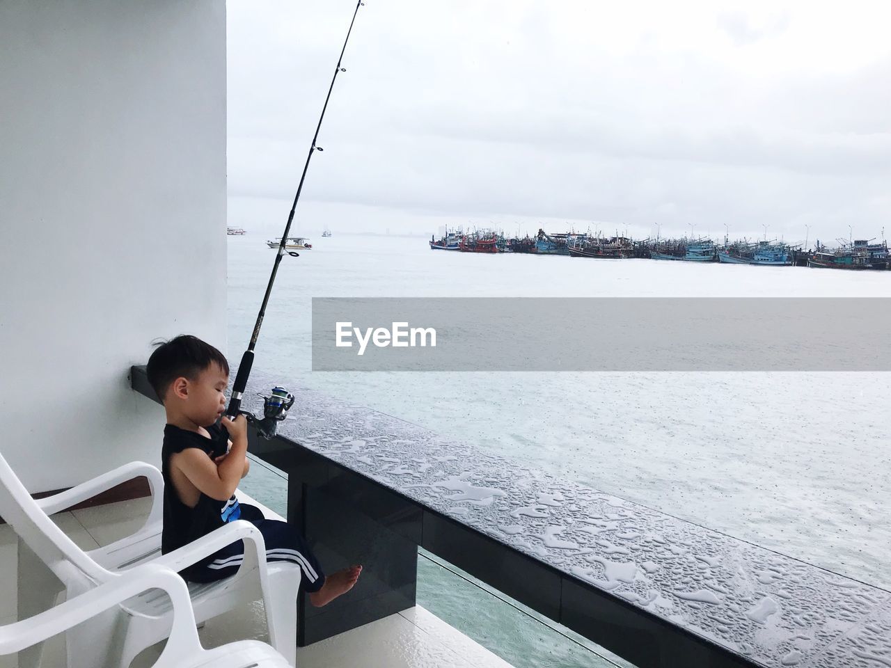 Cute boy fishing while sitting at balcony