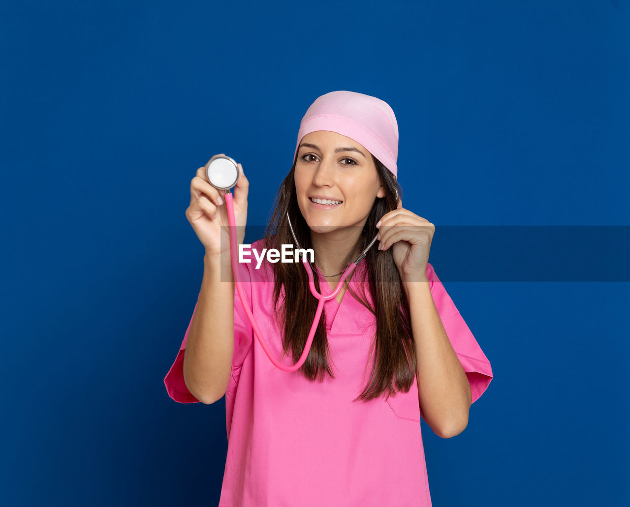 PORTRAIT OF A SMILING YOUNG WOMAN STANDING AGAINST BLUE BACKGROUND